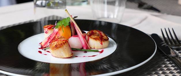 This is a picture of a gourmet dish of sea scallops with lemongrass on a black and white plate.
